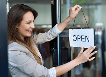 young woman small business owner puts up open sign on her store front